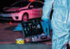 Forensic investigator at crime scene with police car.