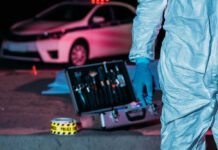 Forensic investigator at crime scene with police car.