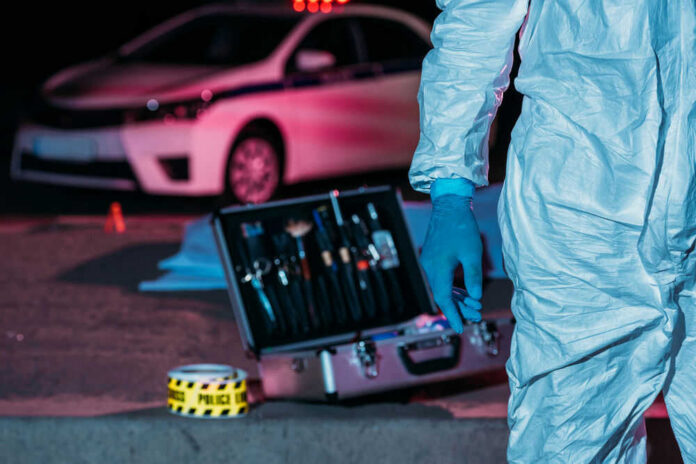 Forensic investigator at crime scene with police car.