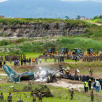 Airport Fireball Sparks Iran Blame Game Airplane crash site with rescue workers and heavy machinery in a grassy field