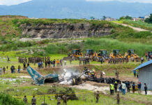 Airport Fireball Sparks Iran Blame Game Airplane crash site with rescue workers and heavy machinery in a grassy field