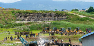 Airplane crash site with rescue workers and heavy machinery in a grassy field