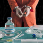 Handcuffed person in orange jumpsuit behind medical equipment