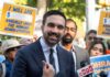 Power Broker Backs America-Is-Disgrace Candidate A man speaking at a rally with supporters holding protest signs
