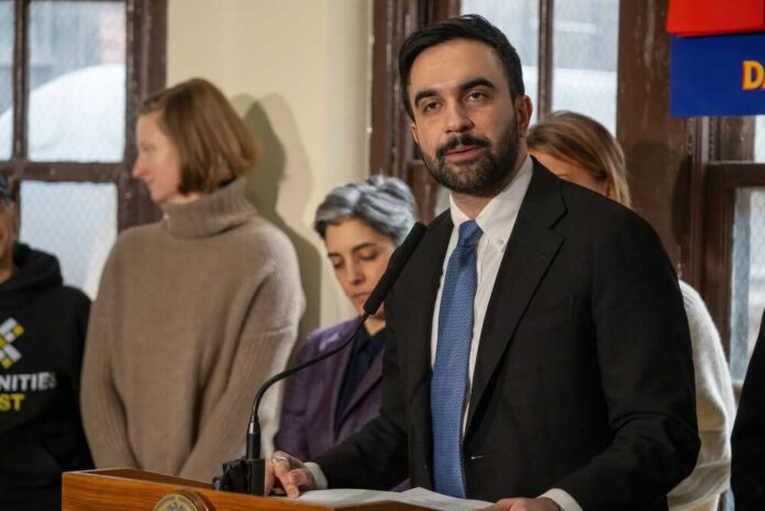 Man in suit speaking at a podium with people standing behind