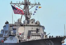 Hormuz Flashpoint: Drones Down, Radar Hit A naval destroyer displaying the American flag and various signal flags