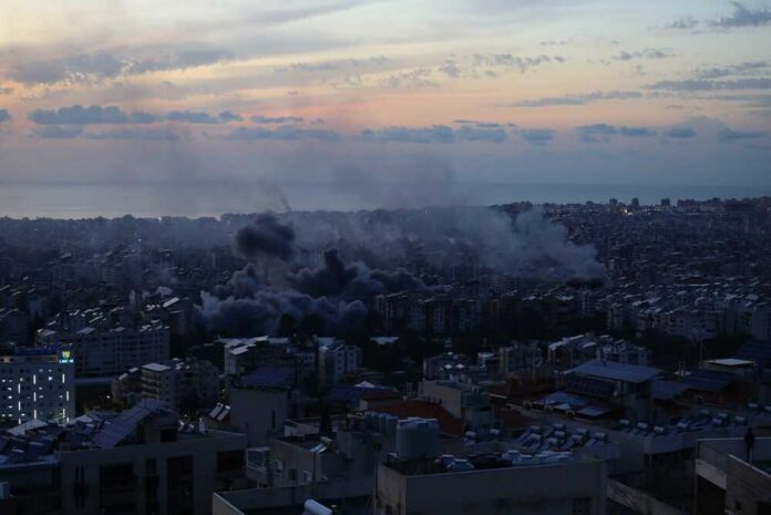 A city skyline at sunset with smoke rising from buildings