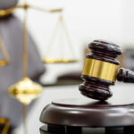 A wooden gavel resting on a sound block with a blurred scale of justice in the background