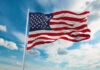 Lindsey Graham Tribute Triggers Backlash American flag waving on a flagpole against a blue sky with clouds