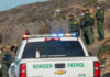 Historic Lows Rattle Immigration Debate Border Patrol officers speaking with individuals near a fence.