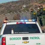 Historic Lows Rattle Immigration Debate Border Patrol officers speaking with individuals near a fence.