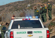 Historic Lows Rattle Immigration Debate Border Patrol officers speaking with individuals near a fence.