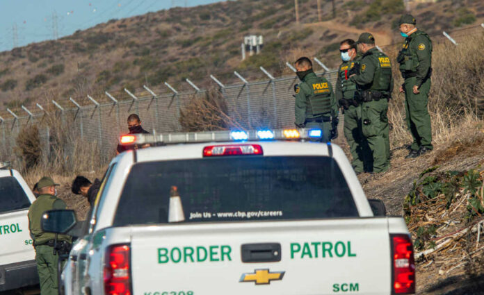 1900868446jpeg Border Patrol officers speaking with individuals near a fence.