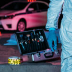 Forensic investigator at crime scene with police car.