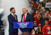 TRUMP Bets Big on Pillow King Two men in suits on stage at a crowded political rally