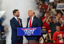 TRUMP Bets Big on Pillow King Two men in suits on stage at a crowded political rally