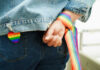 Person wearing rainbow ribbon and heart pin on denim