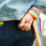 Person wearing rainbow ribbon and heart pin on denim
