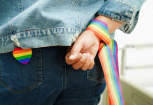 Person wearing rainbow ribbon and heart pin on denim