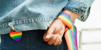 Person wearing rainbow ribbon and heart pin on denim