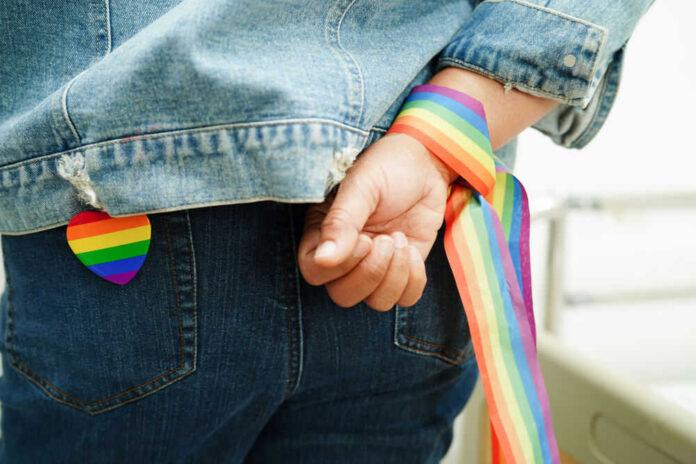 lgbt-665949998 Person wearing rainbow ribbon and heart pin on denim