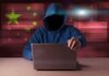 Hooded figure using a laptop with red cybersecurity graphics
