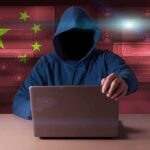 Hooded figure using a laptop with red cybersecurity graphics