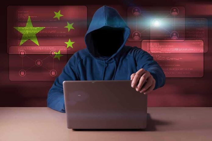 shutterstock_1007210323 Hooded figure using a laptop with red cybersecurity graphics