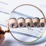 Magnifying glass highlighting wooden blocks spelling fraud on an invoice