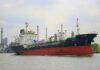Hormuz Shock: Tanker Hit, Markets Twitch A cargo ship navigating through a port with industrial buildings in the background