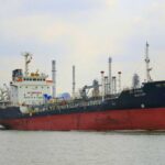 Hormuz Shock: Tanker Hit, Markets Twitch A cargo ship navigating through a port with industrial buildings in the background