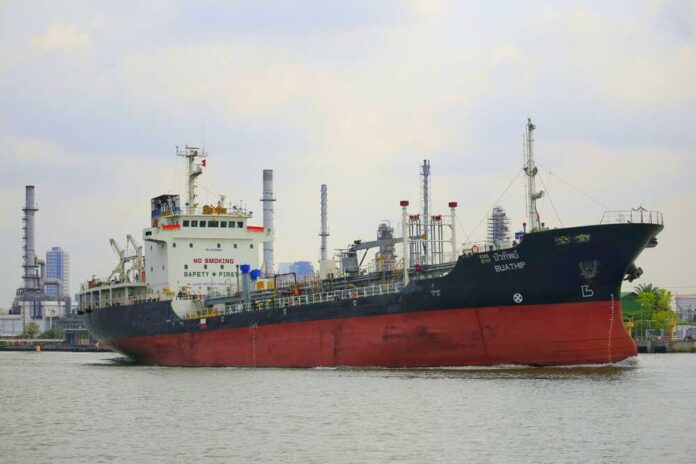 Iran,27,Feb2026:iran,Closes,The,Strait,Of,Hormuz,,Through,Which A cargo ship navigating through a port with industrial buildings in the background