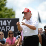 Man in red cap and white golf shirt gesturing at a golf event