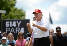 Man in red cap and white golf shirt gesturing at a golf event