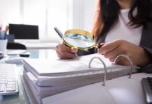 Person using a magnifying glass to review documents in a binder
