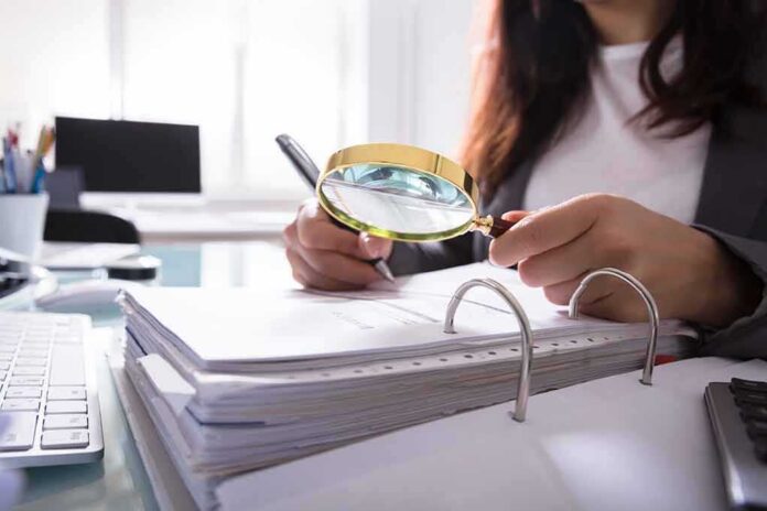 Person using a magnifying glass to review documents in a binder