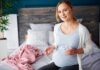 Pregnant woman sitting on bed holding pills and a glass of water