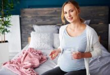 Pregnant woman sitting on bed holding pills and a glass of water