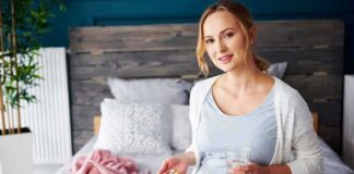 Pregnant woman sitting on bed holding pills and a glass of water