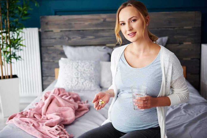 Pregnant woman sitting on bed holding pills and a glass of water