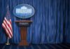 White House press briefing podium with U.S. flag and blue curtain