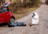 forensic investigator photographing evidence near red car on dirt road