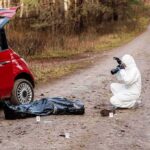 forensic investigator photographing evidence near red car on dirt road