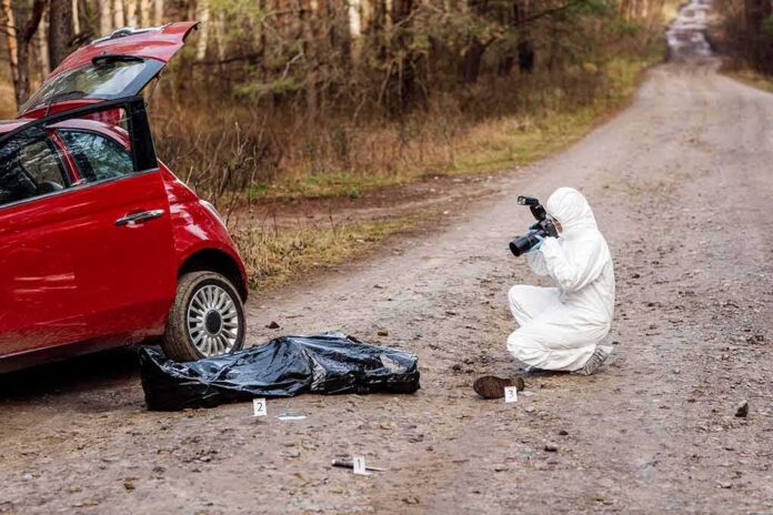 forensic investigator photographing evidence near red car on dirt road