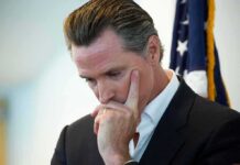 Bait-And-Switch? Newsom’s Managed ‘Disclosure’ man in suit touching his face thoughtfully