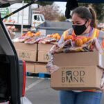Volunteer loads food bank box with produce into car trunk