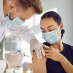 Healthcare worker giving a masked patient a vaccine in the upper arm
