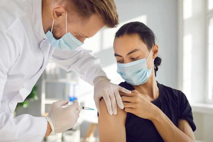 shutterstock_1903346662-1 Healthcare worker giving a masked patient a vaccine in the upper arm
