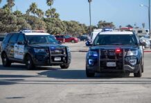Two police SUVs with lights on in a coastal parking lot