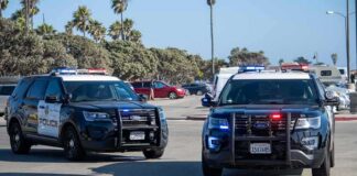 Two police SUVs with lights on in a coastal parking lot
